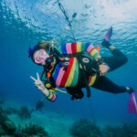 a diver dressed as rainbow bright poses under water flashing the peace sign during a halloween event dive in roatan.