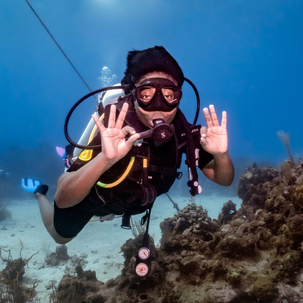 A woman diver gives the double 'ok' sign to show she's having a great time on her Discover Scuba Diving experience in Roatan.