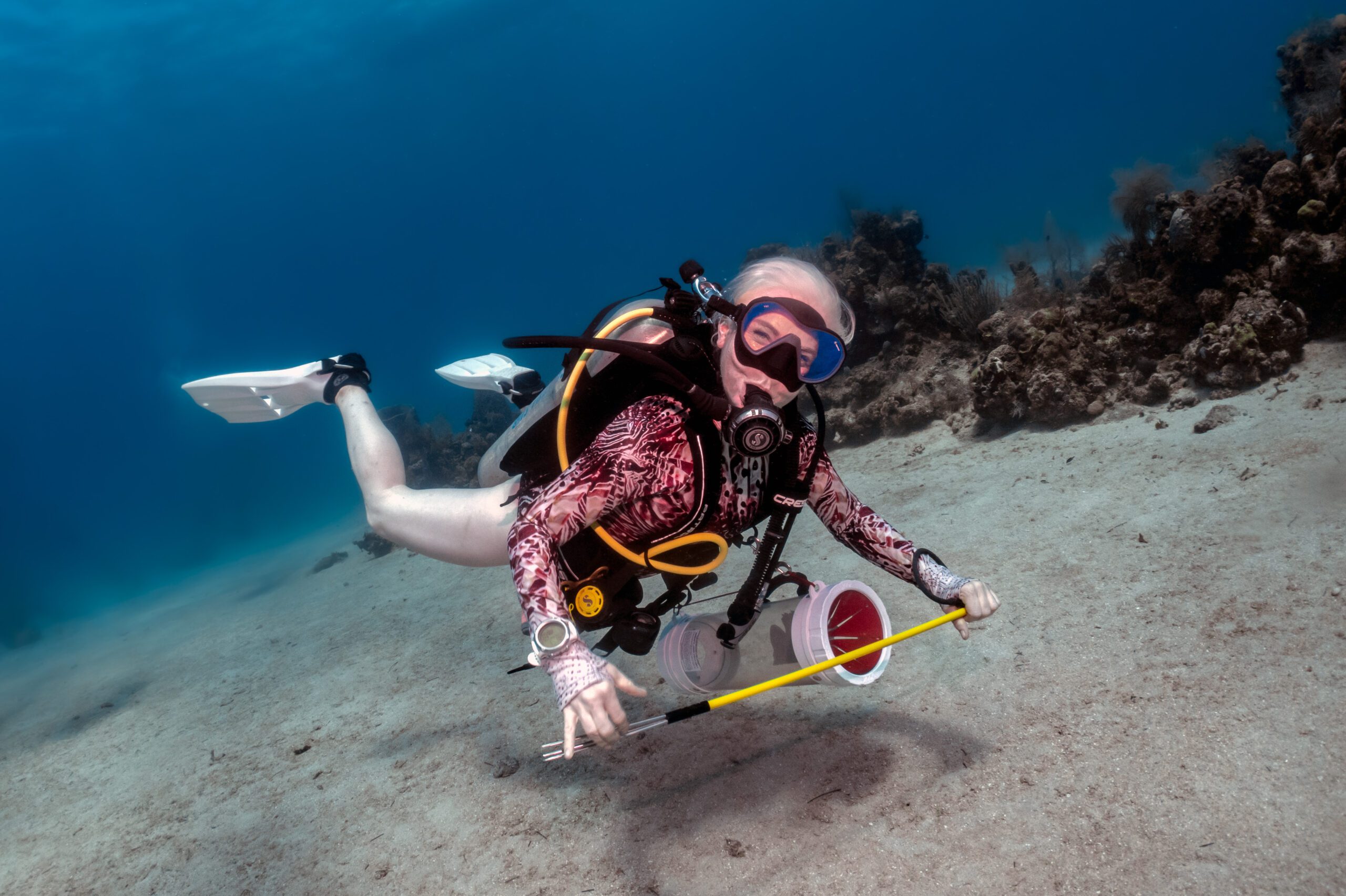 A woman is scuba diving with a lion fish container and spear in her hands.