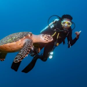 A young boy throws up the hang ten sign while diving right to a sea turtle on his open water dive in Roatan, Honduras. 
