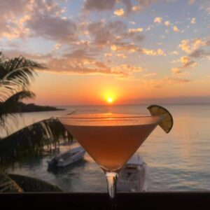 A tropical martini with a lime wedge is silhouetted by the sunset in Half Moon Bay, West End, Roatan. 