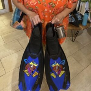A woman holds her colourfully painted scuba fins for diving into the camera.