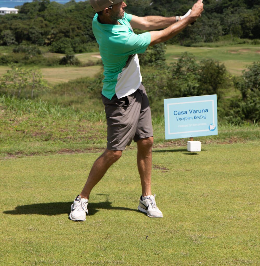 A golfer in a green golf shirt in mid swing. 