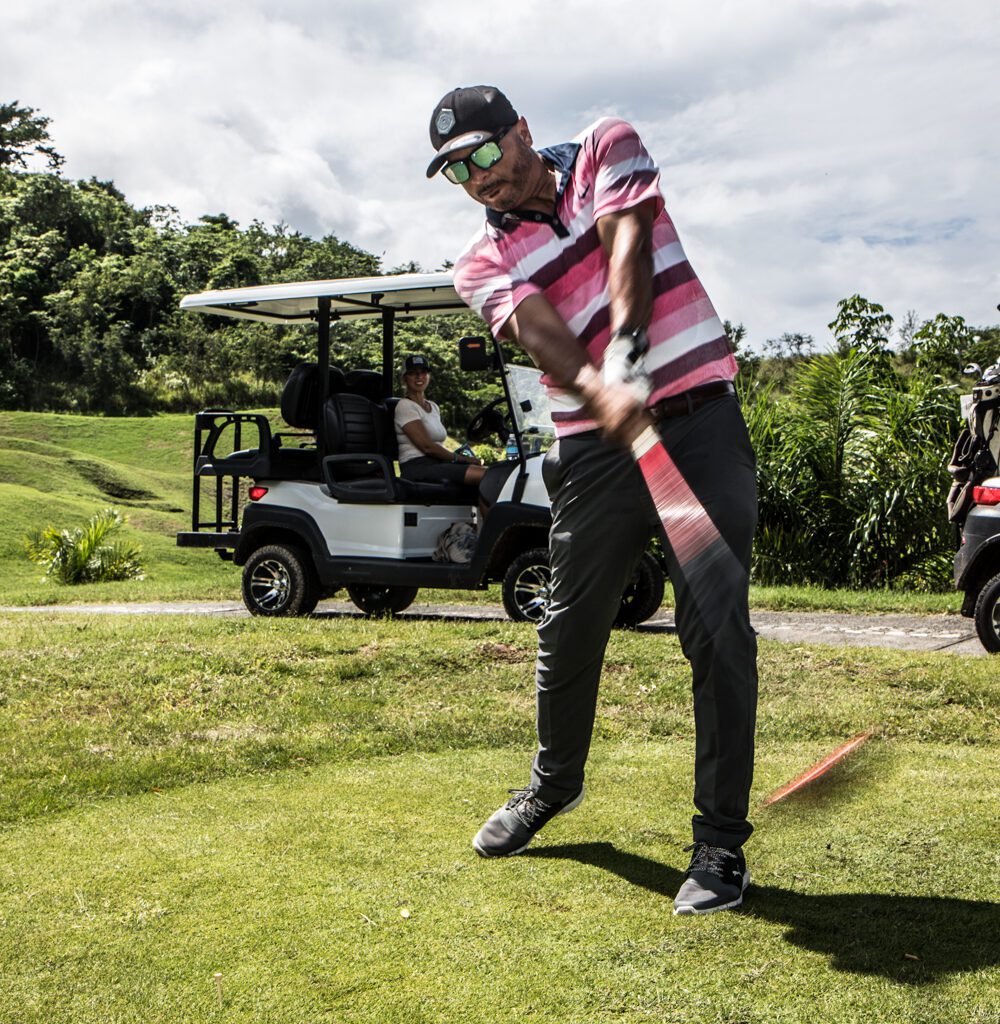 A golfer in a red, white an black striped golf shirt captured mid-swing. 