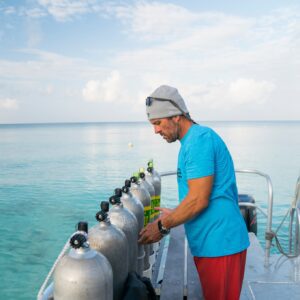A man in a blue shirt is adding nitrox stickers to scuba diving tanks on a boat. 