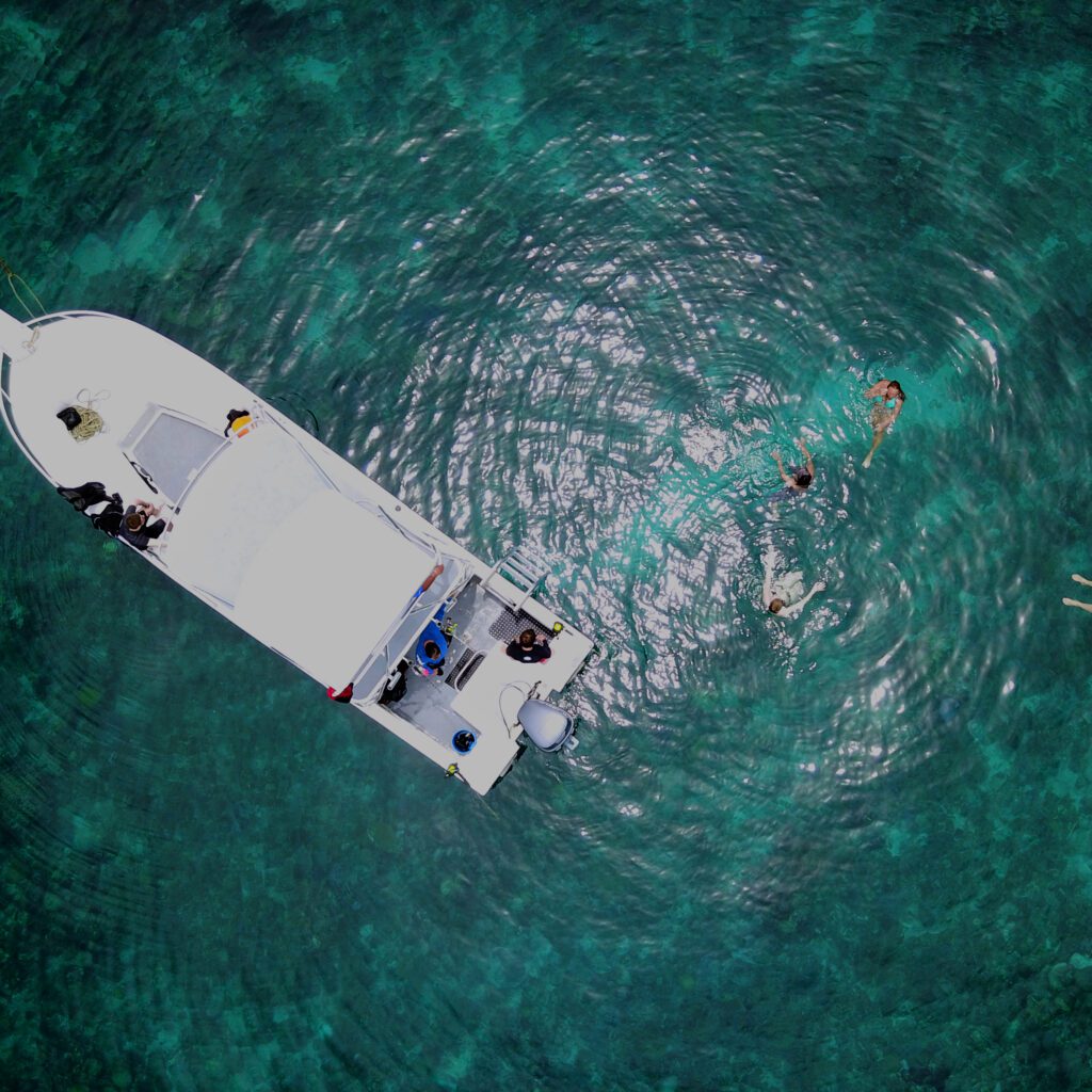 The Sun Divers boat is photographed from a bird eye perspective and you can see people floating in the crystal clear waters around the boat during their surface interval in between scuba dives in Roatan.