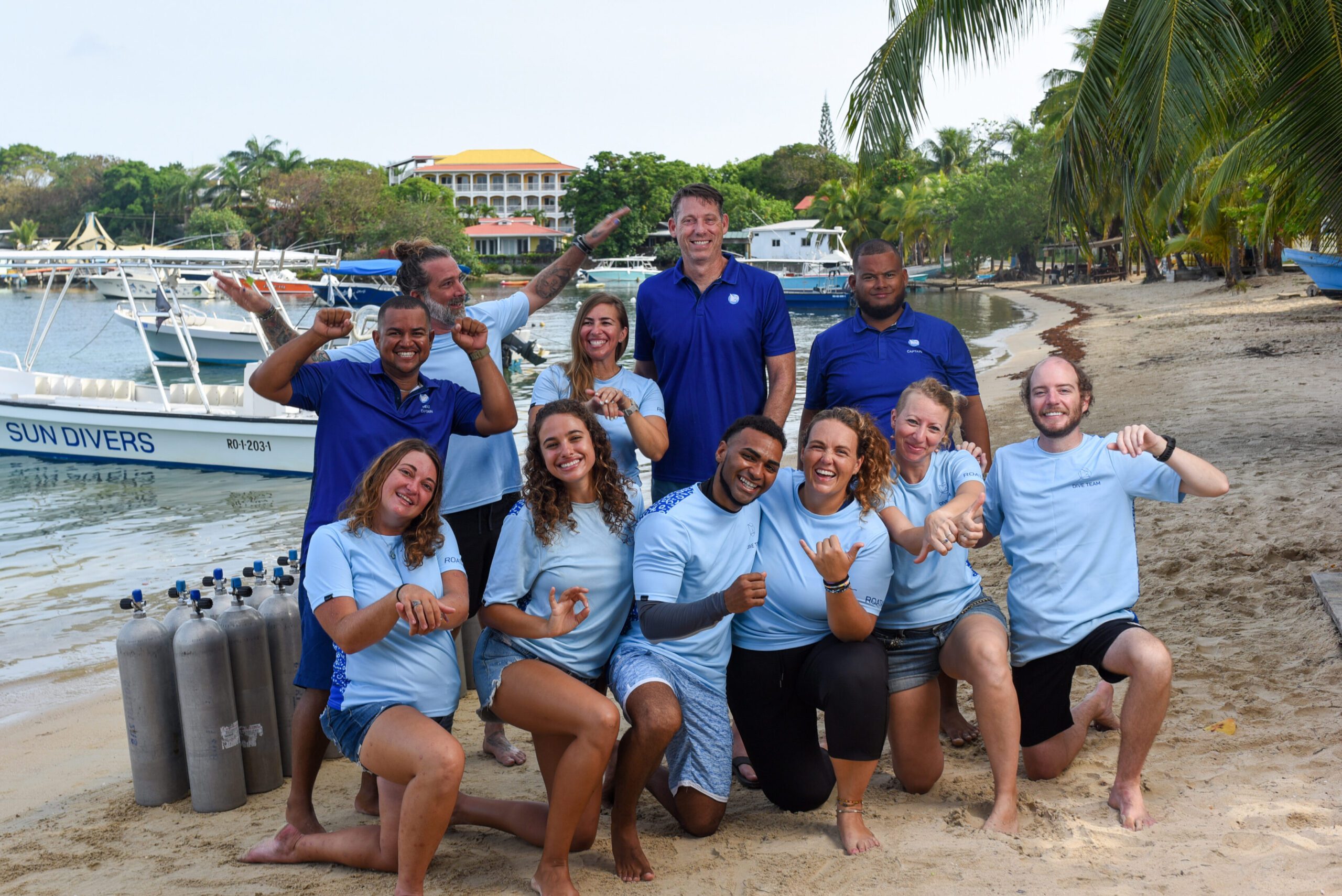 The team of the dive shop Sun Divers Roatan is wearing their team shirts and standing at the beach in front of the diver centers boats in Roatan, Honduras.