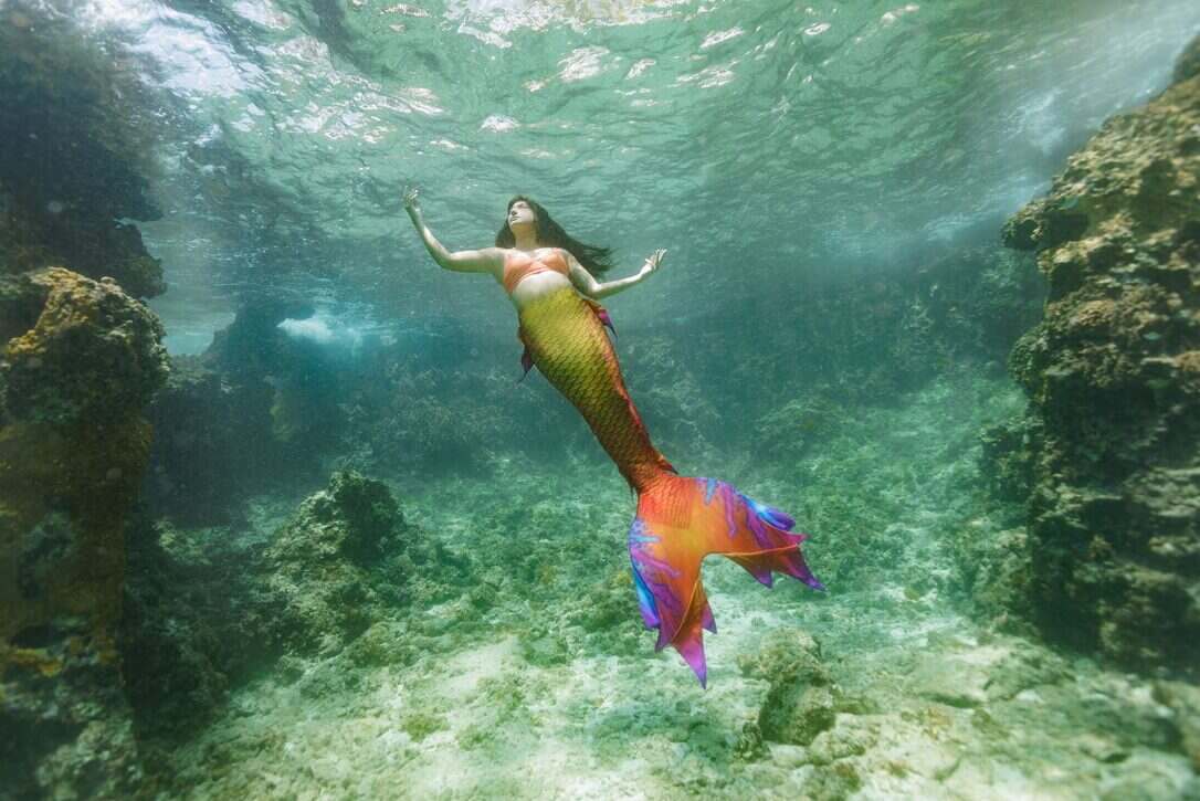 PADI Mermaid instructor Alanna  ascends to the surface with her pink, purple and orange tail tailing behind her