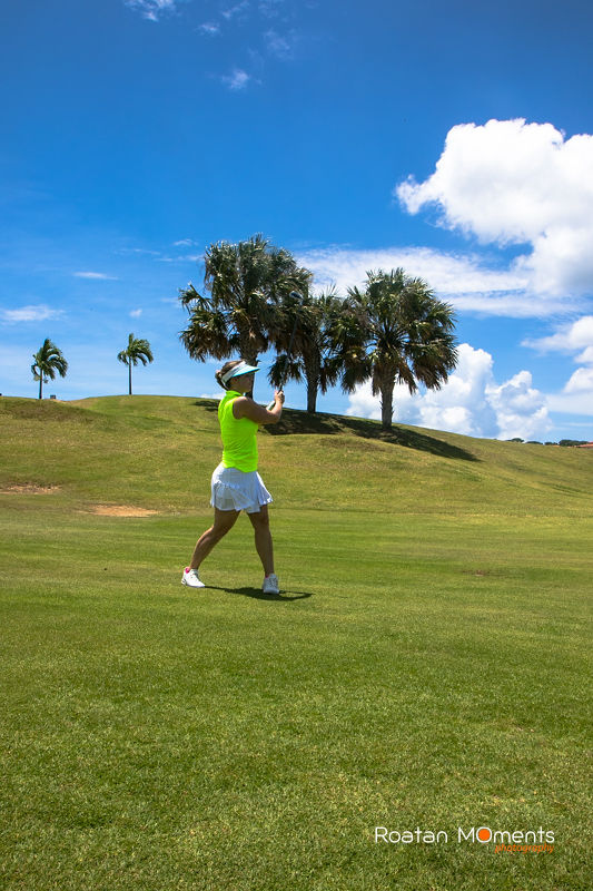 Woman golfer take a swing in front of large palm trees at Pristine bay In Roatan. 