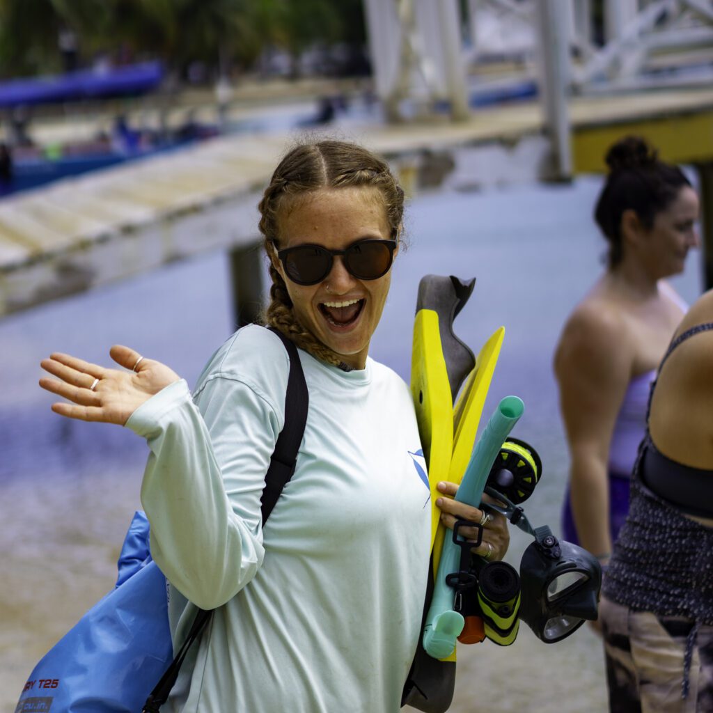 A girl with pig tails strikes a pose as she walks to the water with her fins and mask to snorkel at PADI Women's Dive Day in Roatan