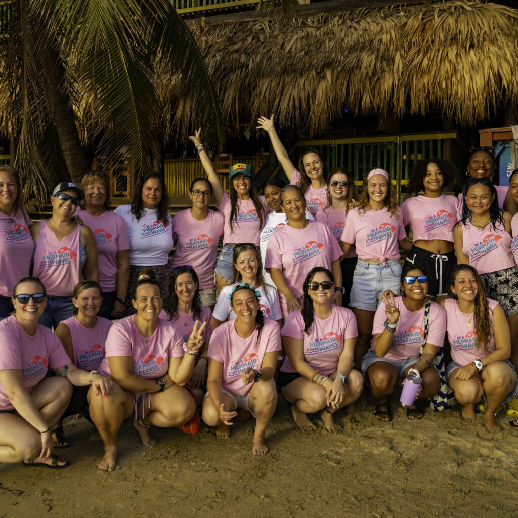 Group photo of women wearing pink PADI Women's Dive day shirts on the beach. 