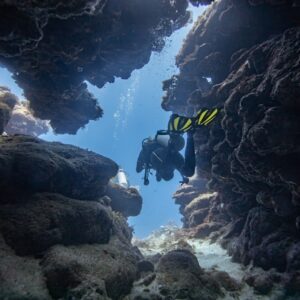 At the Spooky Channel dive site in Roatan, a diver with yellow fins makes there way through a swim through exiting toward the blue.
