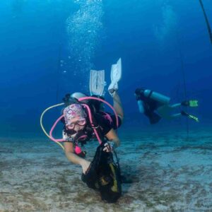female diver in pink puts a piece of trash in a mesh bag during a dive against debris in roatan