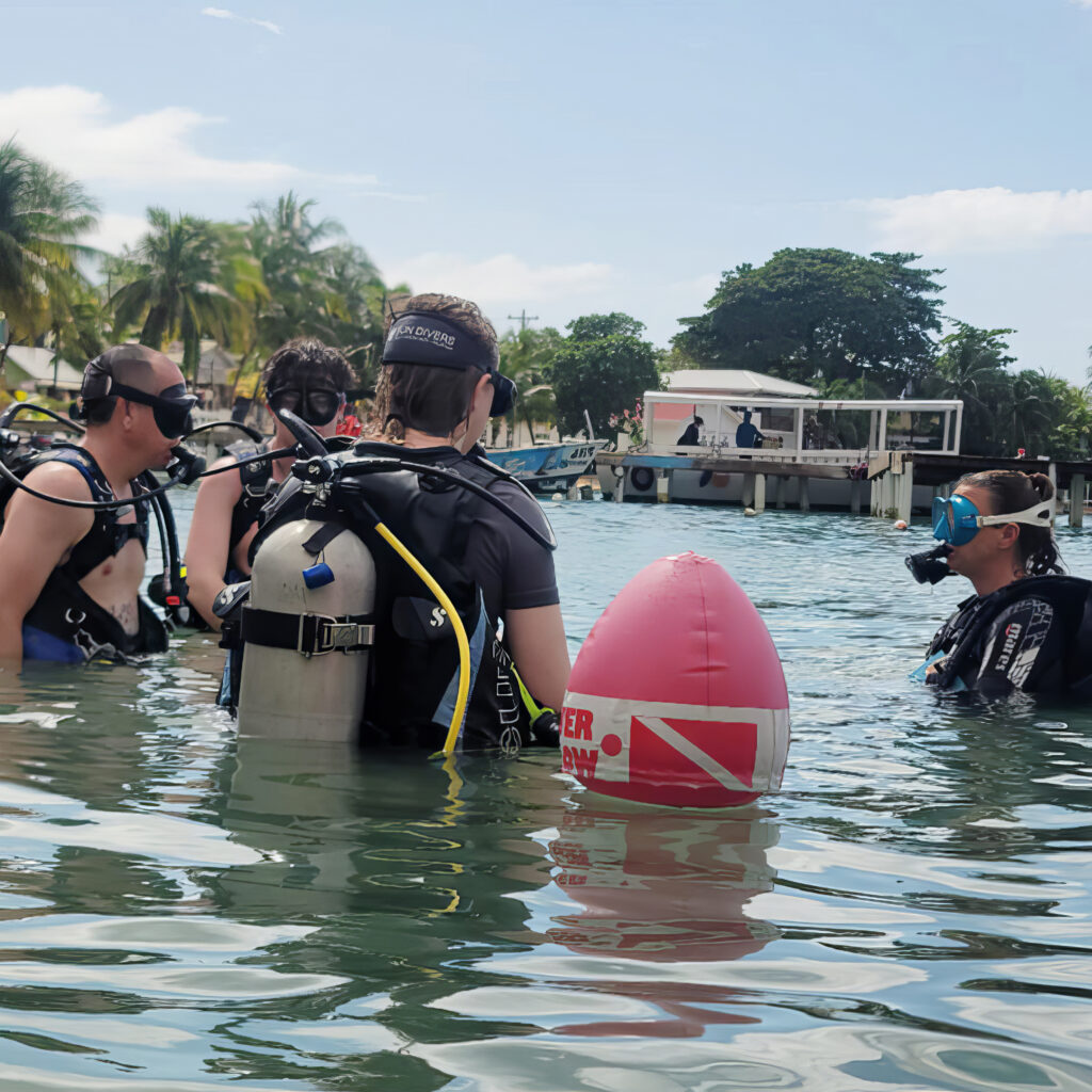 A family stands in the water with regulators in their mouth preparing to scuba dive for the first time in roatan.
