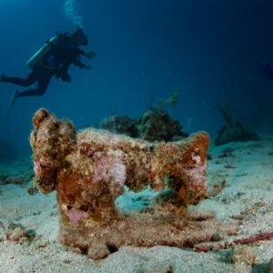An old Singer sewing machine sits on the bottom of a sandpatch encrusted with coral and marine life at Butchers Bank, a beginner dive site. Roatan, Honduras.
