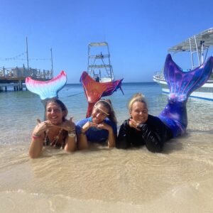Three PADI mermaid students pose on the beach with their tails flipped in the air